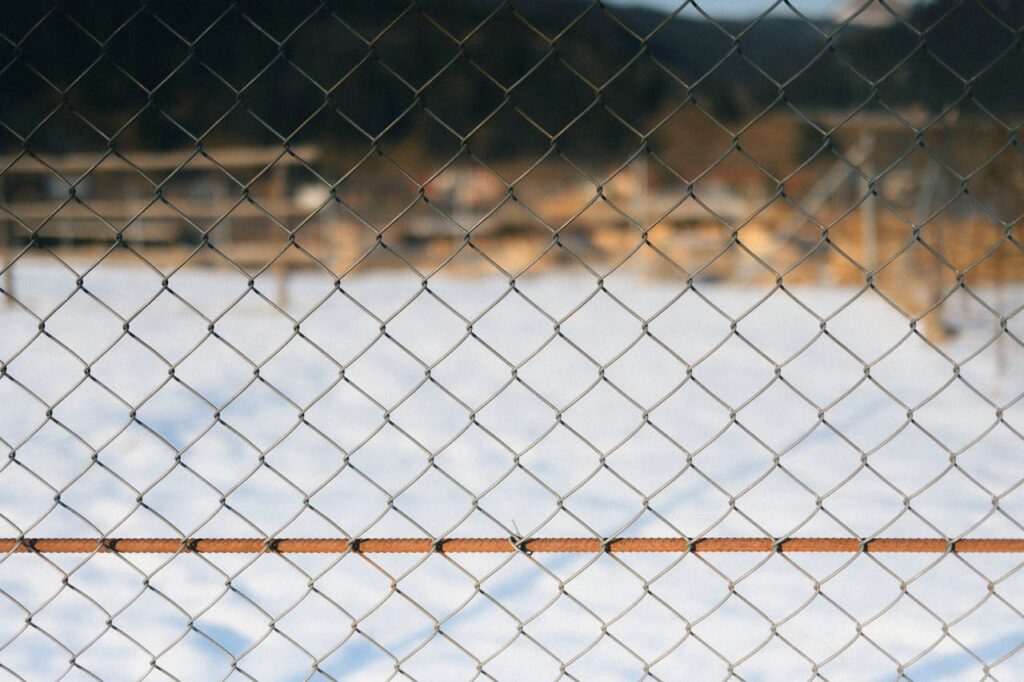 A chain link fence in sharp focus with a soft snowy backdrop, capturing a serene winter scene.